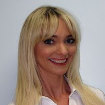 Professional headshot of smiling woman with blonde hair in white shirt against light background.
