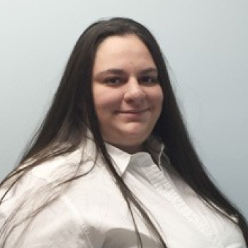 Professional portrait of woman with long dark hair wearing white shirt against neutral background.