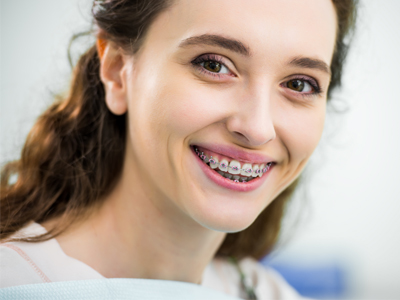 Young woman smiling at camera displaying braces in bright clinical orthodontic setting.