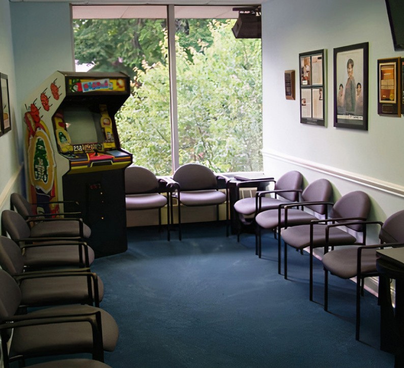 Waiting room at Blue Wave Orthodontics with arcade game, chairs, and large windows overlooking trees.