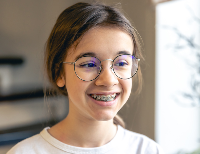 Smiling teenager wearing purple-framed glasses and white shirt in modern indoor setting.