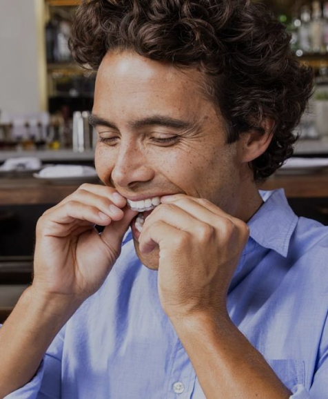 Man in blue shirt examining teeth with fingers in dental office setting.