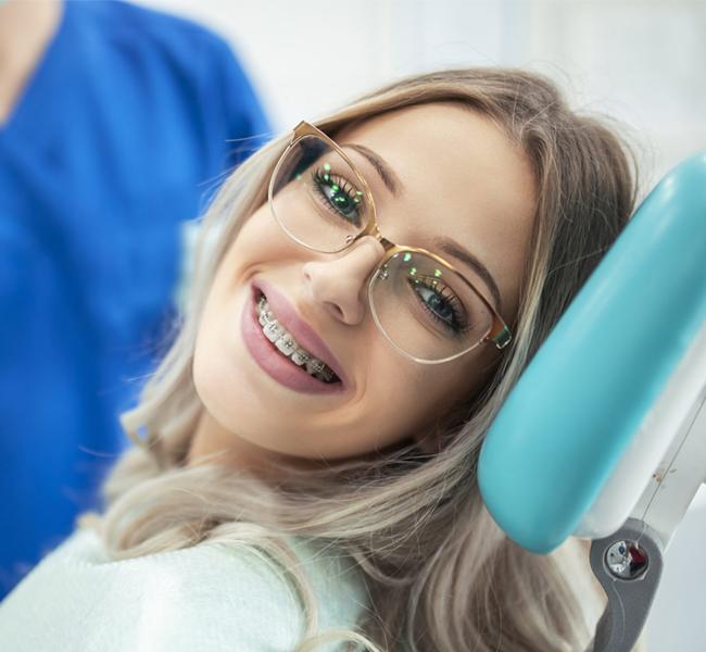Young woman in orthodontic chair wearing glasses, smiling during dental examination at Blue Wave Orthodontics.