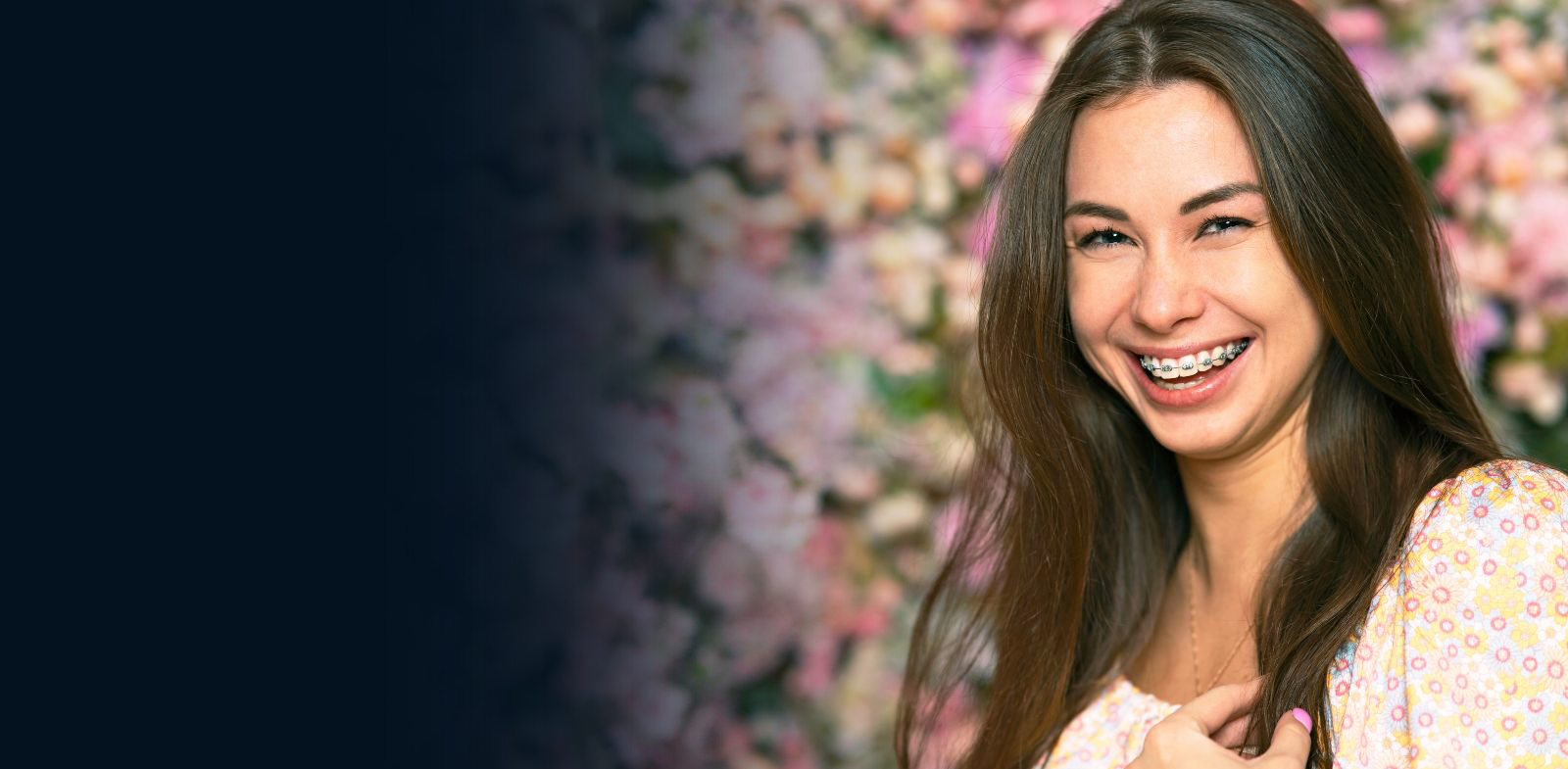 Smiling woman with long dark hair against floral backdrop at orthodontics office