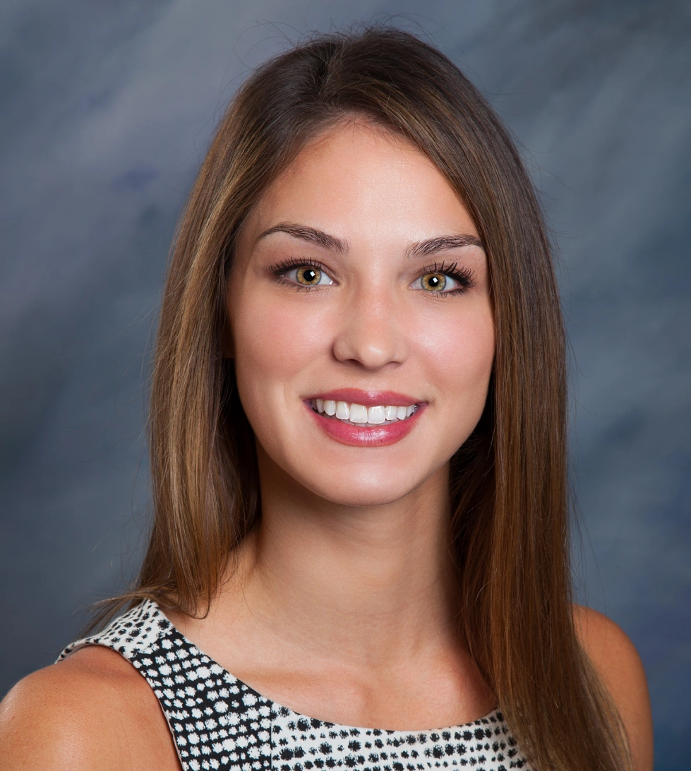 Professional headshot of smiling woman with long brown hair against blue background for orthodontics practice.