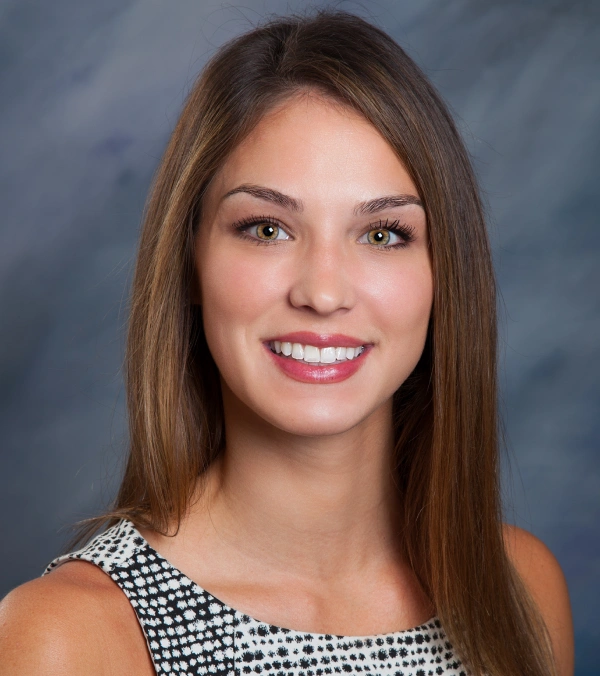 Professional portrait of smiling woman with long brown hair against blue background for orthodontics practice.