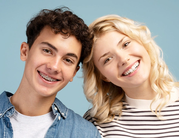 Two smiling teenagers with healthy teeth against a blue background, promoting orthodontic care.