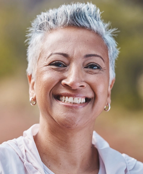 Smiling woman with short white hair wearing pearl earrings in outdoor setting.