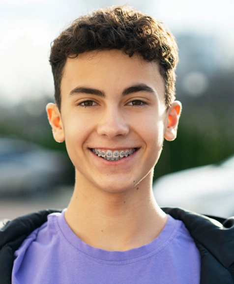 Young person smiling wearing purple shirt with braces, outdoor blurred background